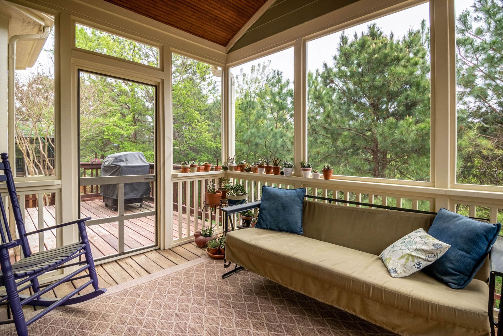 Screened porch with a hinged screen door to the deck, a sofa and a rocking chair, where screen door repair keeps bugs out
