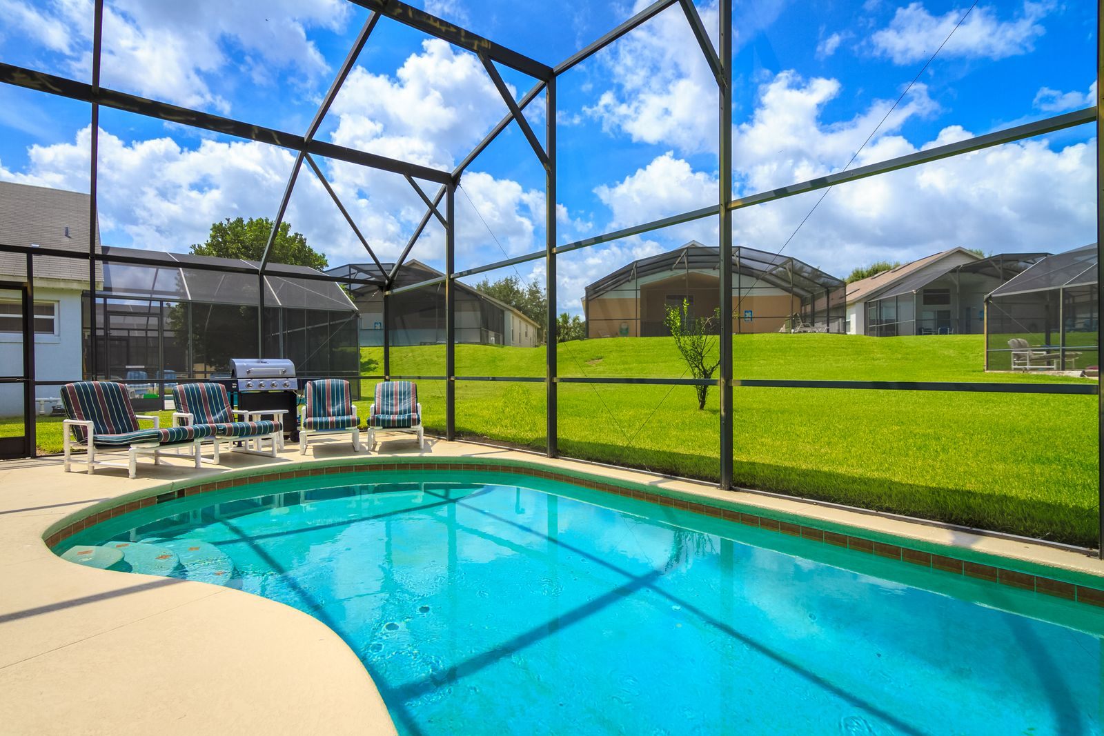 Florida backyard pool inside an aluminum-framed screen enclosure, with lounge chairs and neighboring screened pools beyond - the kind of cage that needs screen repair over time
