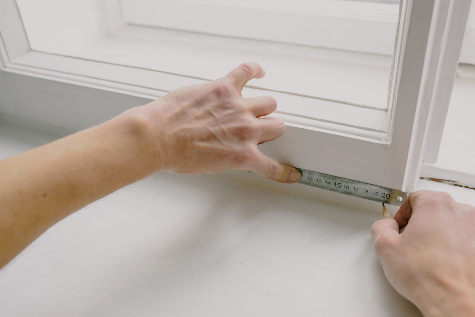 Hands measuring a white window frame with a metal ruler before cutting new screen from a screen repair kit