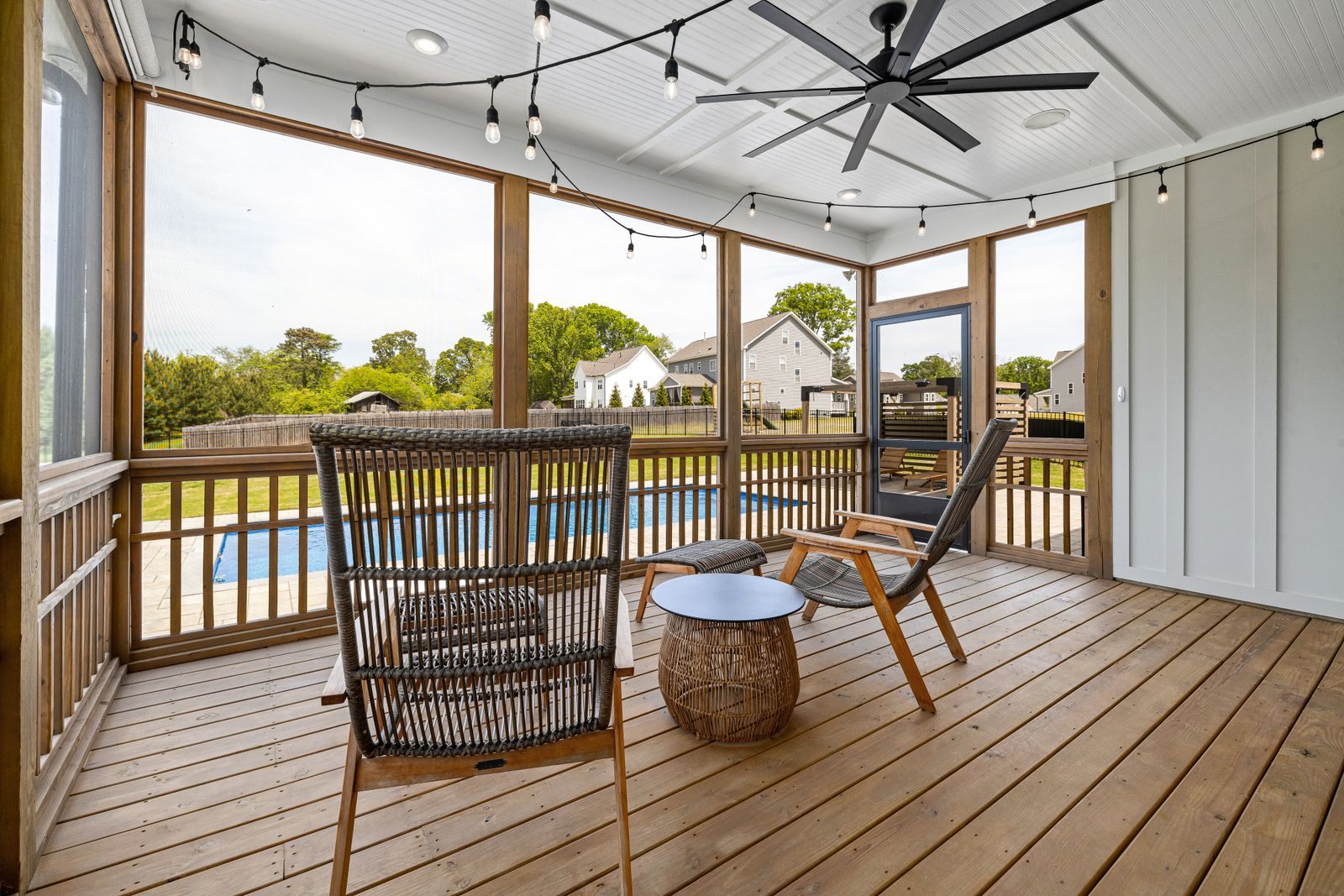 Screened porch with wicker chairs and a ceiling fan looking out to a backyard pool through the screen panels